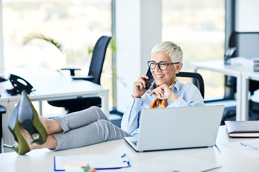 Client Center - Senior Businesswoman Makes a Call, Smiling With Her Feet up on the Desk
